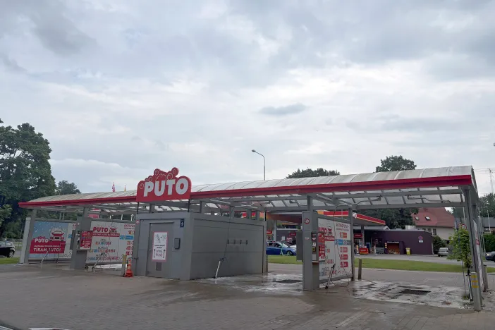 Auto mazgātava ar jumtu, sarkaniem akcentiem un mākoņainu debesu fona.