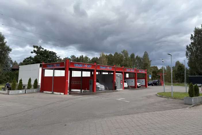 Sarkana automazgātuve ar vairākām mazgā&scaron;anas zonām zem mākoņainām debesīm.