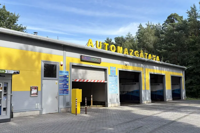 Automa&scaron;īnu mazgātuve ar dzeltenu fasādi un trīs garāžas durvīm.