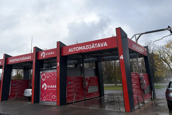 Automazgātava ar sarkanu un melnu dizainu, pelēks debess fons.