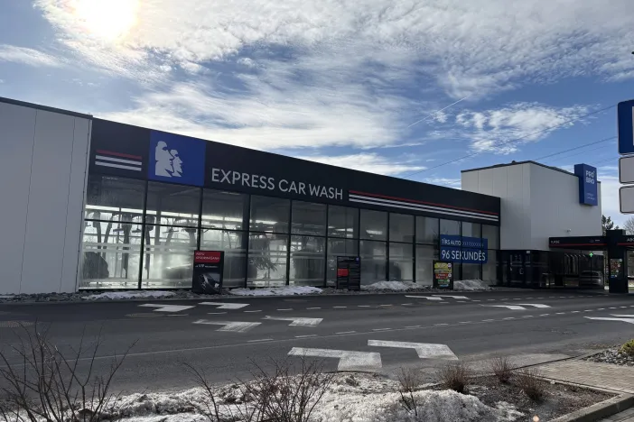 Express automazgātava ēka ar stiklotu fasādi saulainā dienā.