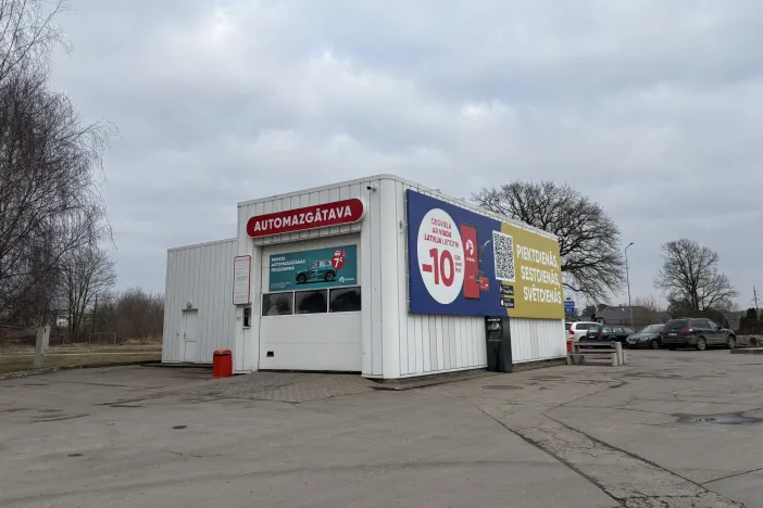 Automazgātava pelēkā dienā ar reklāmu uz sienas.