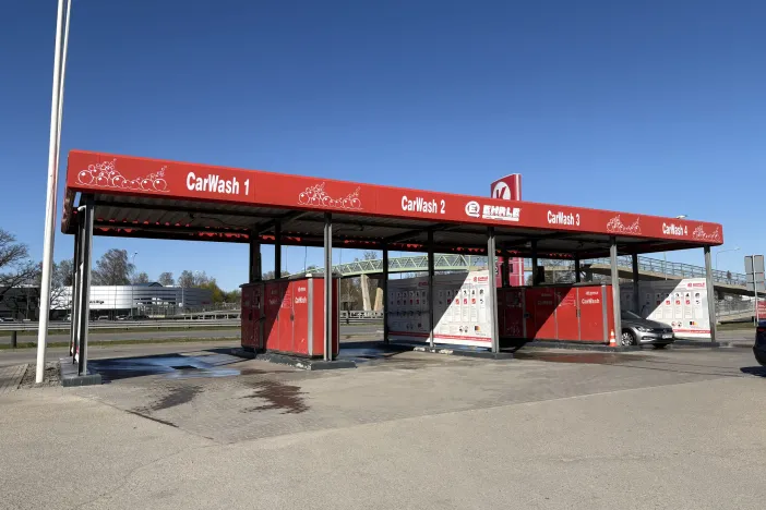 Sarkanā automazgātuve ar četriem boksiem un zilu debesu fona.