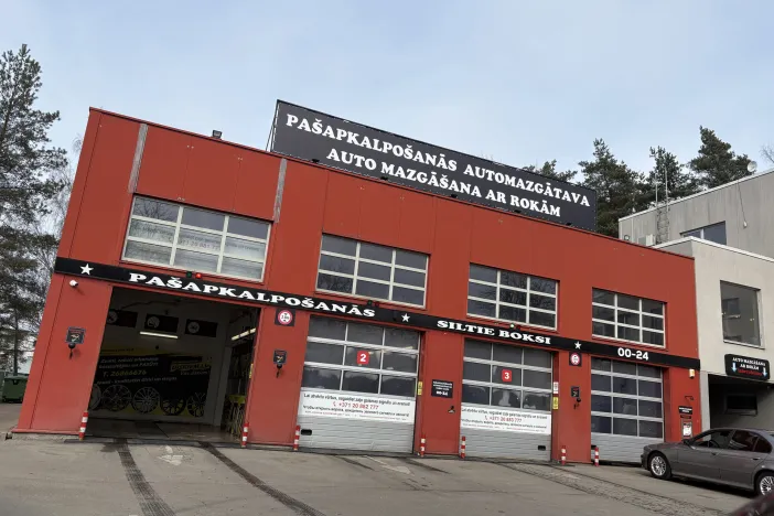 Automazgātavas ēka ar sarkanu fasādi un vairākām garāžas durvīm.
